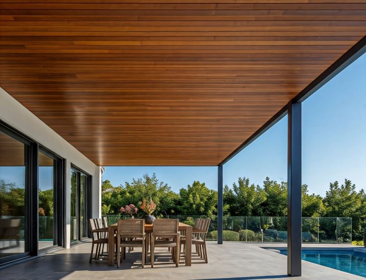 Modern alfresco patio with wooden ceiling, dining table, and pool in the background.
